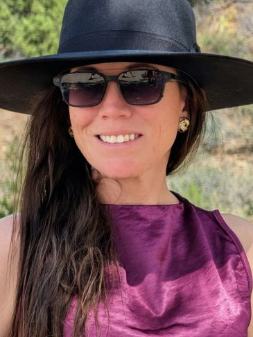 Woman smiling with black hat and sunglasses.