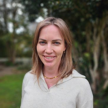 Headshot of Ashleigh standing in a garden. Ashleigh has light brown hair, blue eyes and a warm smile