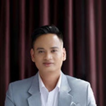 Portrait of a man in a light gray suit against a dark curtain background.