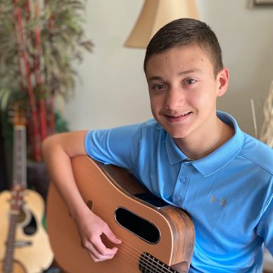 Smiling boy in blue shirt playing an acoustic guitar indoors.
