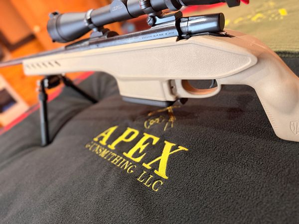 A scoped rifle resting on a black Apex Gunsmithing LLC cloth.
