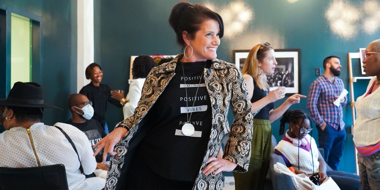 A woman smiling confidently in a patterned jacket at a lively social gathering indoors.