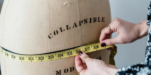 Hands measuring a vintage dress form with a yellow tape measure.