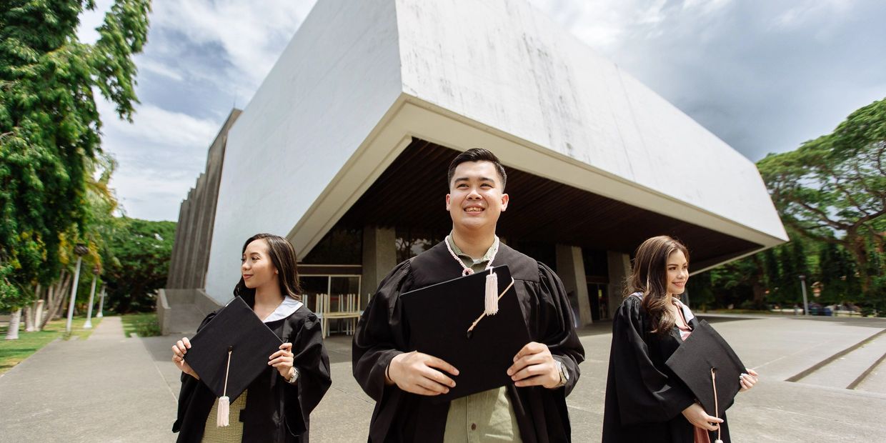 Three graduates holding caps outside a modern building.