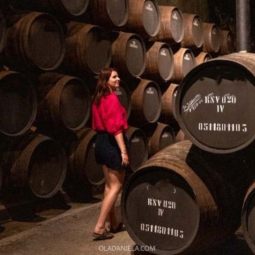 Mulher em adega com barris de vinho.