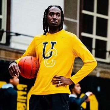 Man in yellow sweatshirt holding a basketball on a basketball court.