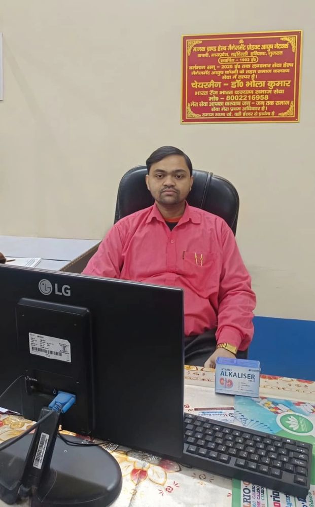 Man in red shirt sitting at desk with computer in office.