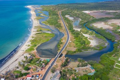 A coastal road running alongside a river and beach with surrounding greenery.
