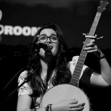 Woman playing banjo and singing into a microphone.
