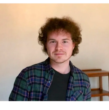 Young man with curly hair smiling indoors.