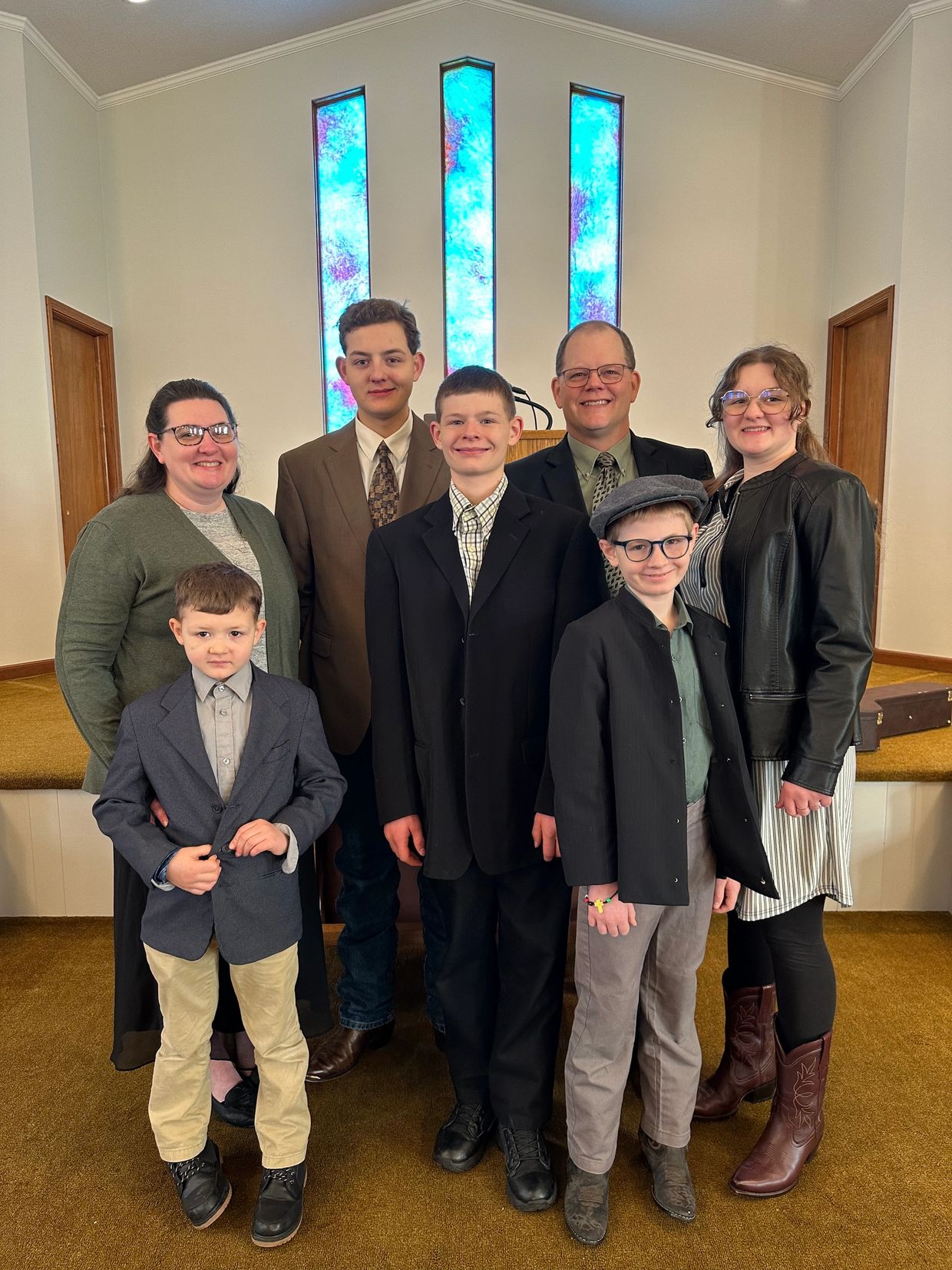 A family dressed formally, standing inside a church with stained glass windows.
