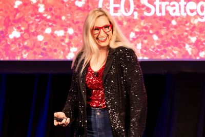 A woman in red and black sparkly outfit speaking on stage with a smile.