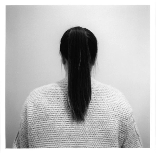 Woman with long hair in a ponytail, seen from behind, wearing a textured sweater.