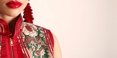 Close-up of a woman wearing a red floral embroidered garment with red tassel earrings and glossy red lipstick.