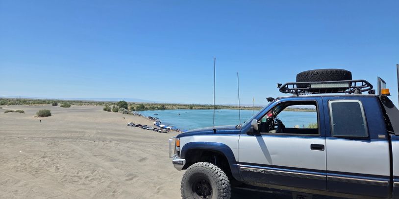 Off-road truck next to a river with sandy terrain.