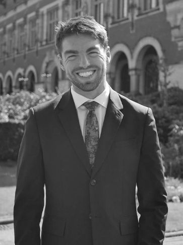 Smiling man in a suit outdoors in front of a historic building.