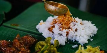 Traditional meal with rice and various side dishes served on a banana leaf.