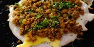 Close-up of a dish with a runny egg topped with spiced minced meat and herbs.