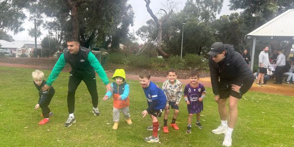 Two men coaching five kids on a grassy field.