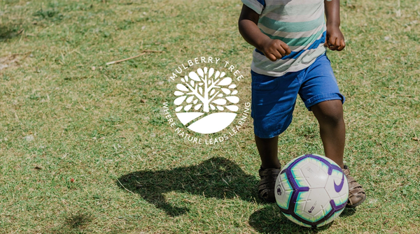 Child playing soccer on grass field.
