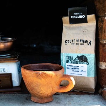 Una taza rústica y una bolsa de café tostado oscuro.