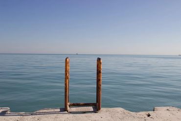 Rusty ladder leading into calm ocean water on a concrete pier.