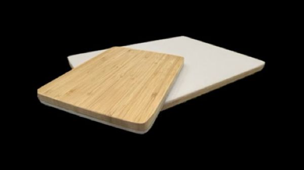 Rectangular wooden cutting board with a white foam pad underneath on black background.