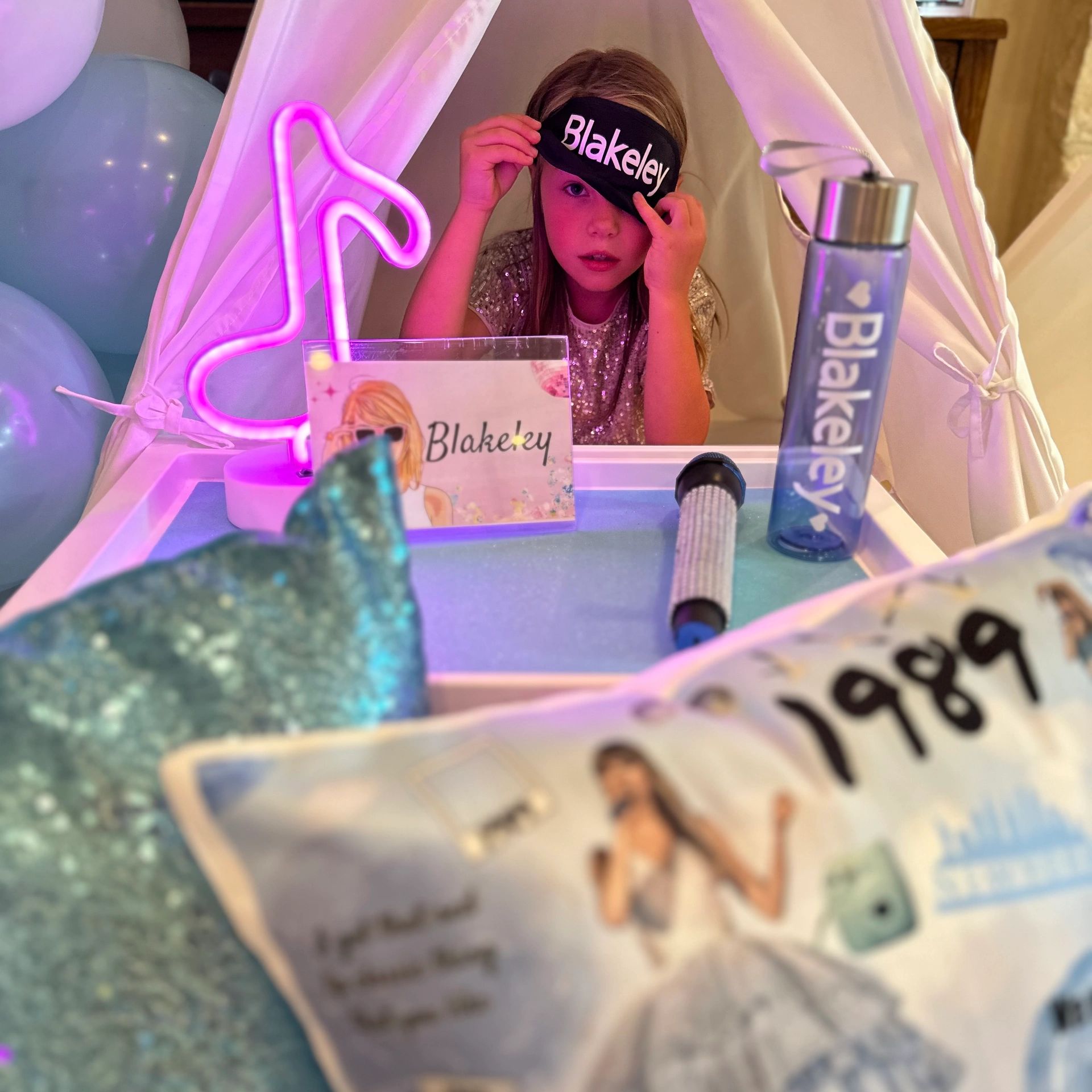 Young girl in a sequined dress wearing a personalized eye mask inside a small tent.