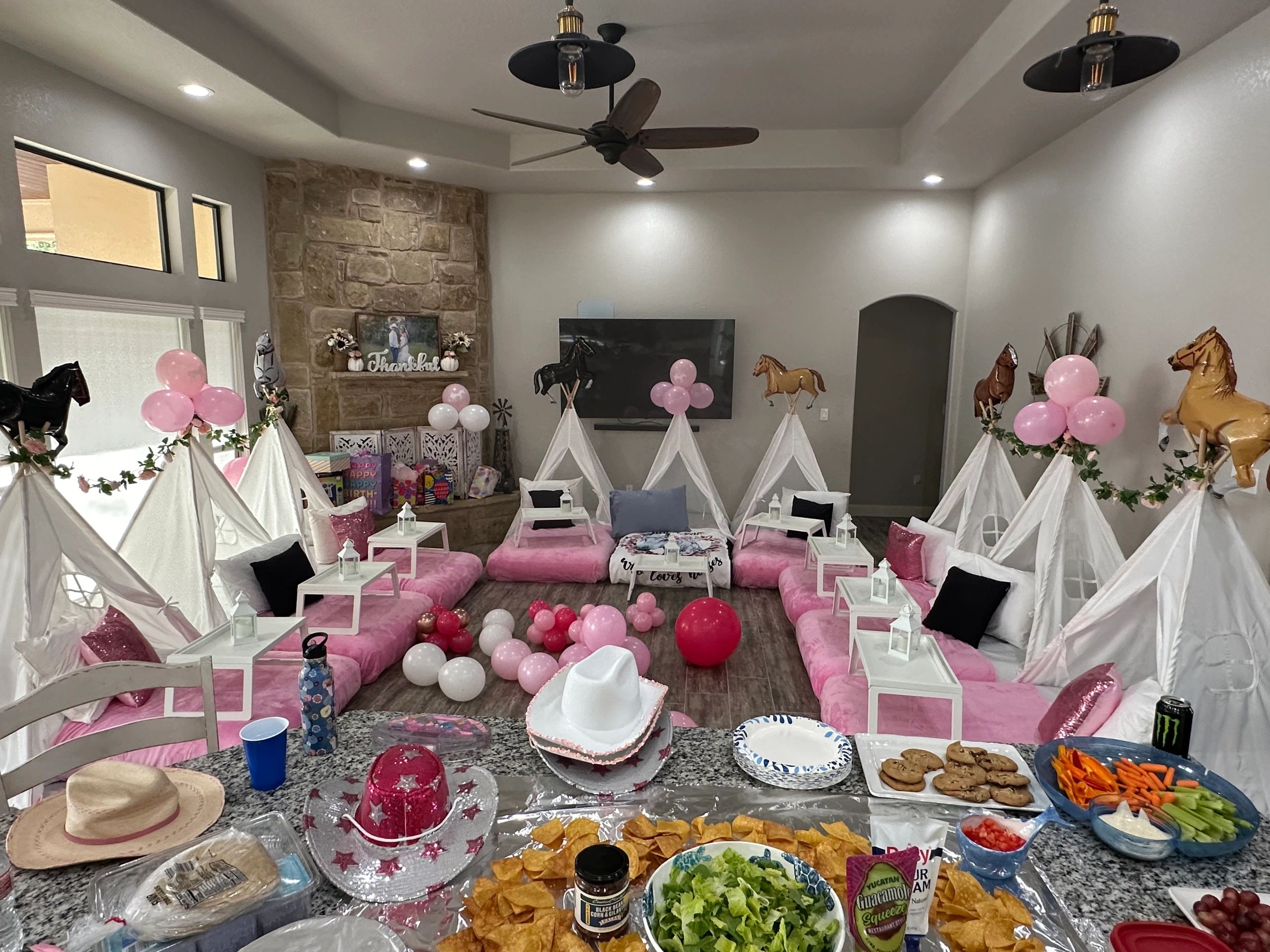 Indoor girls' sleepover party with teepees, pink balloons, and snacks.