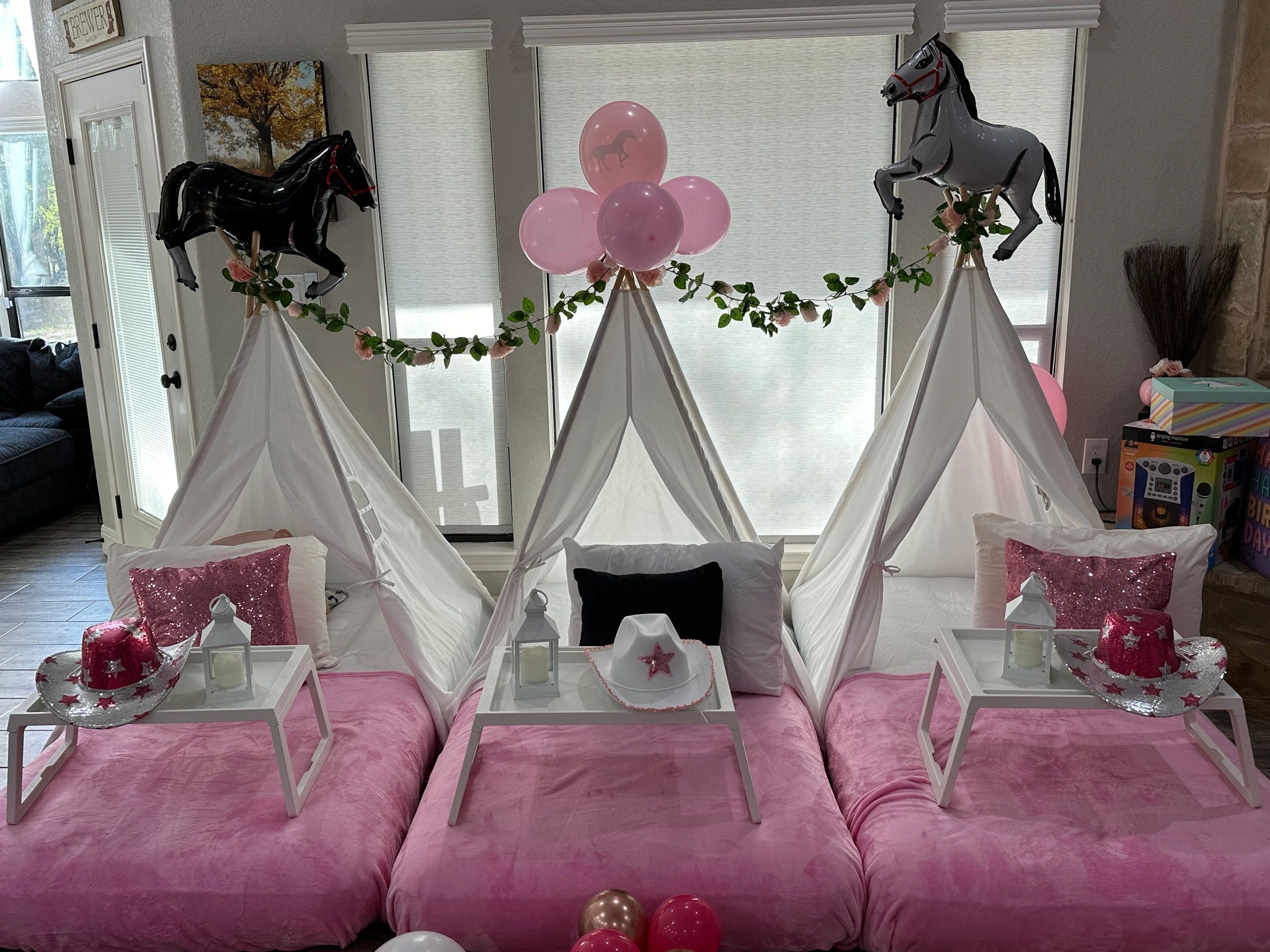 Three teepees decorated with horse balloons and pink bedding for a party.