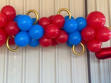 Red and blue balloons intertwined with gold rings against a metal wall.