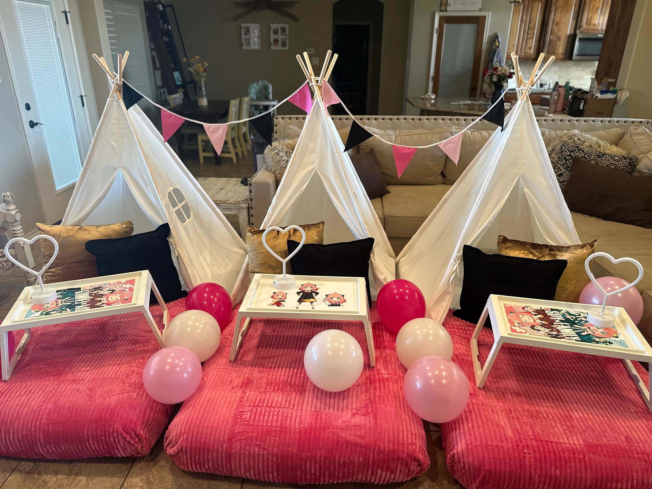 Indoor kids' teepee setup with pink and white balloons and small tables.