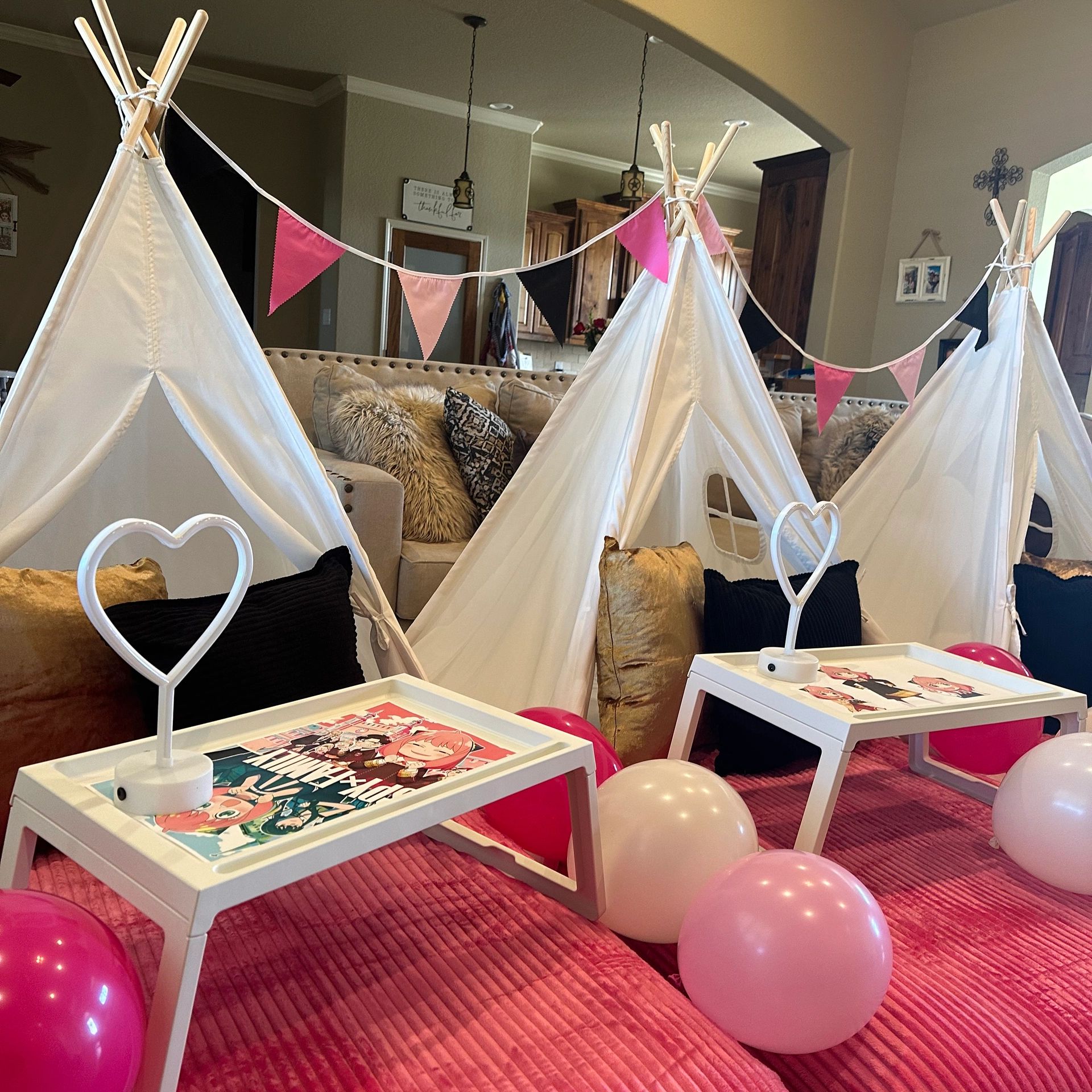Indoor play area with small teepees, balloons, and anime-themed tables on a pink blanket.