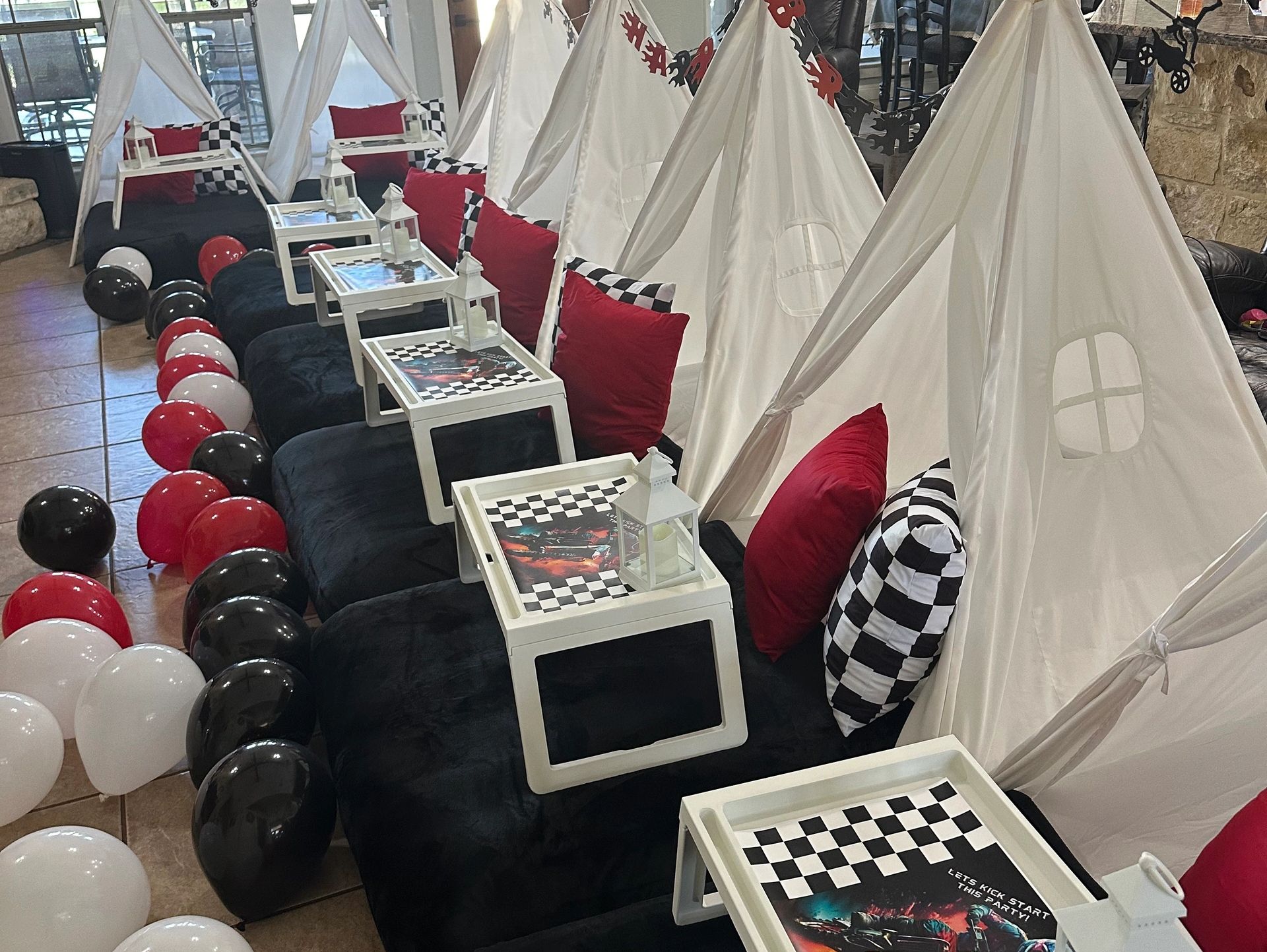 Racing-themed party setup with teepees, checkered pillows, and red, black, and white balloons.