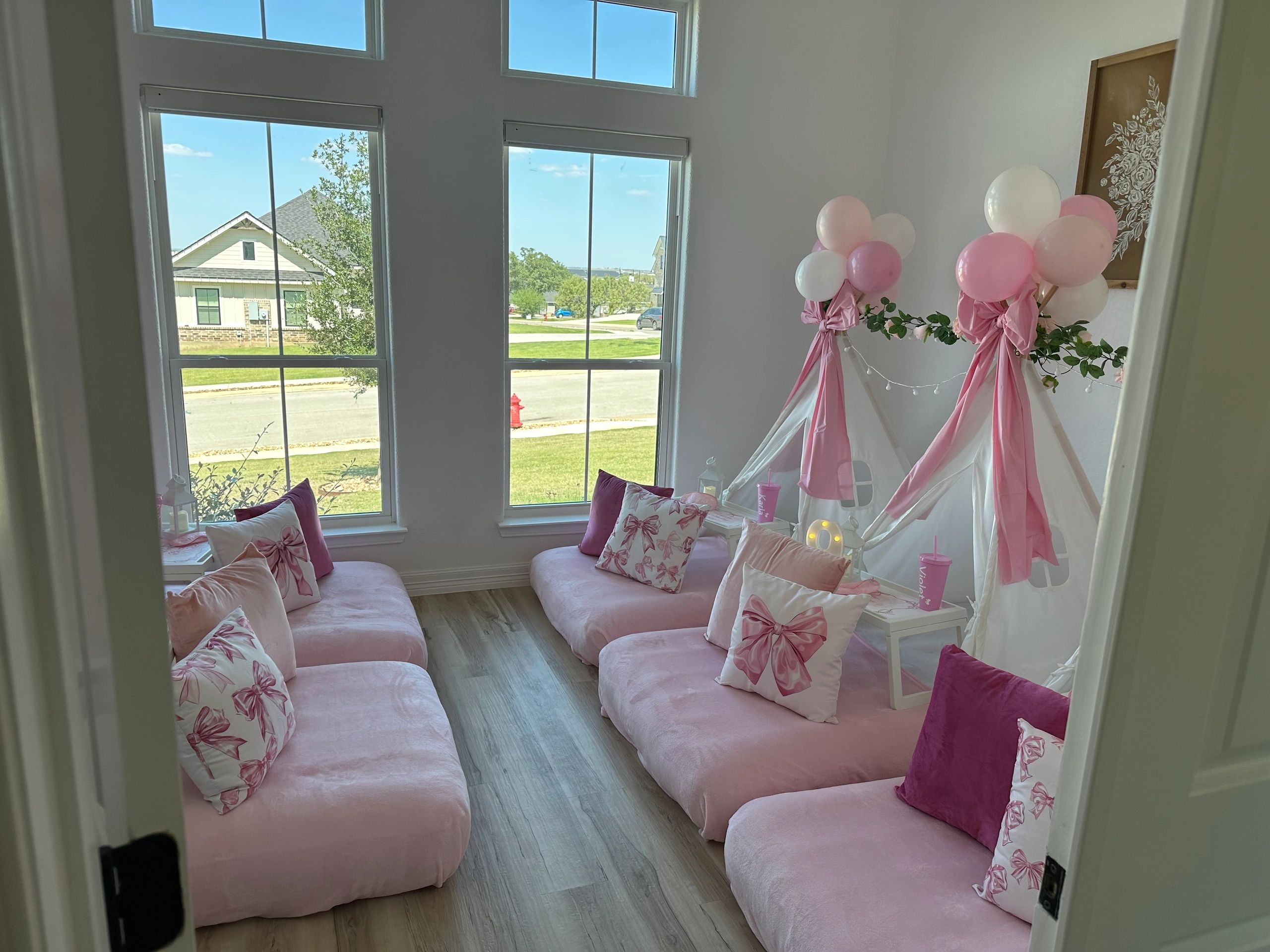 Cozy pink-themed room with cushions, small tents, and balloons by large windows.