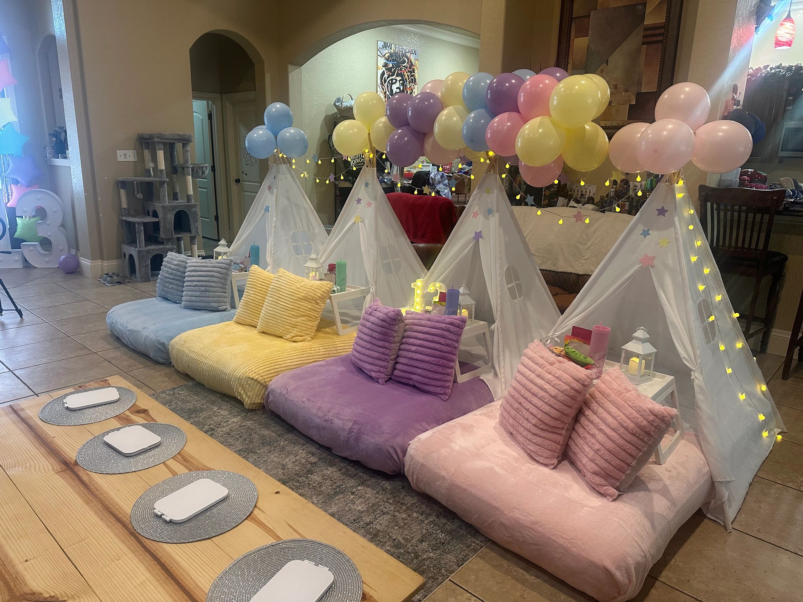 Colorful indoor teepee party setup with balloons and cozy cushions.