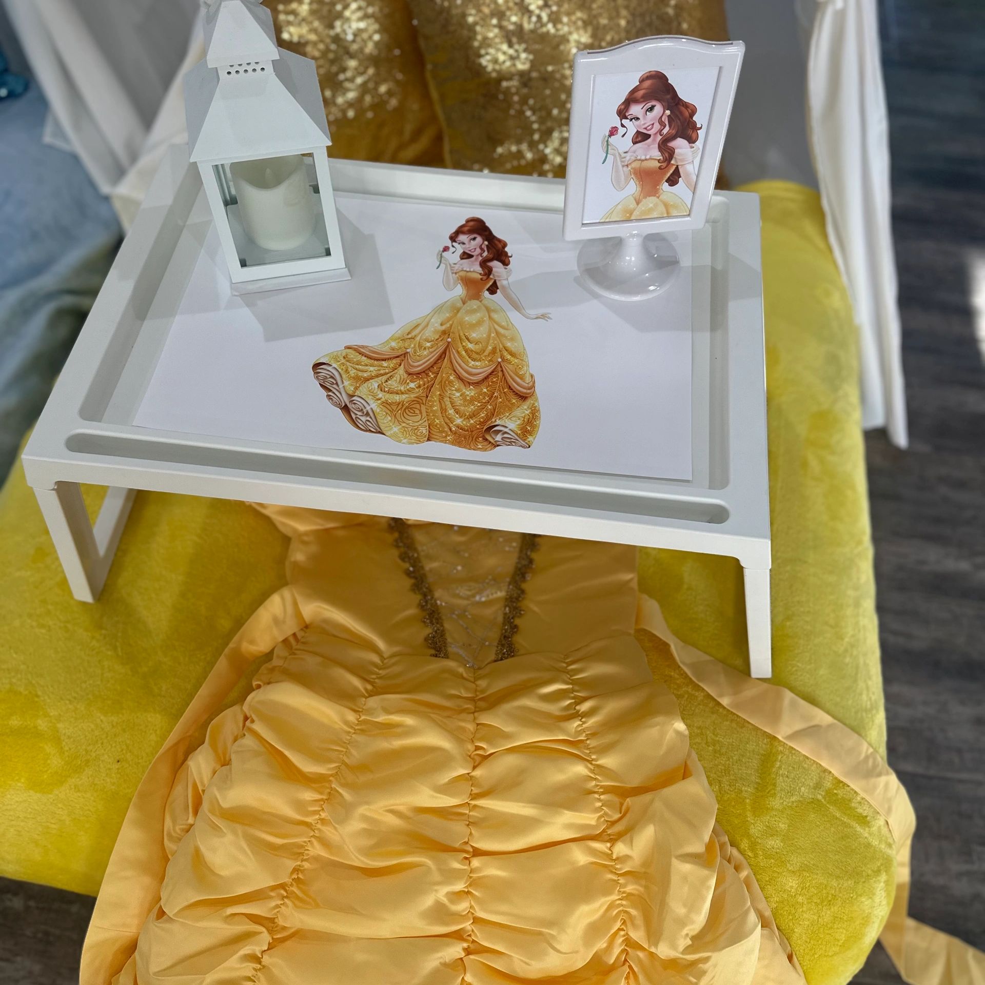 White tray with Belle-themed decorations and yellow dress on a yellow chair.