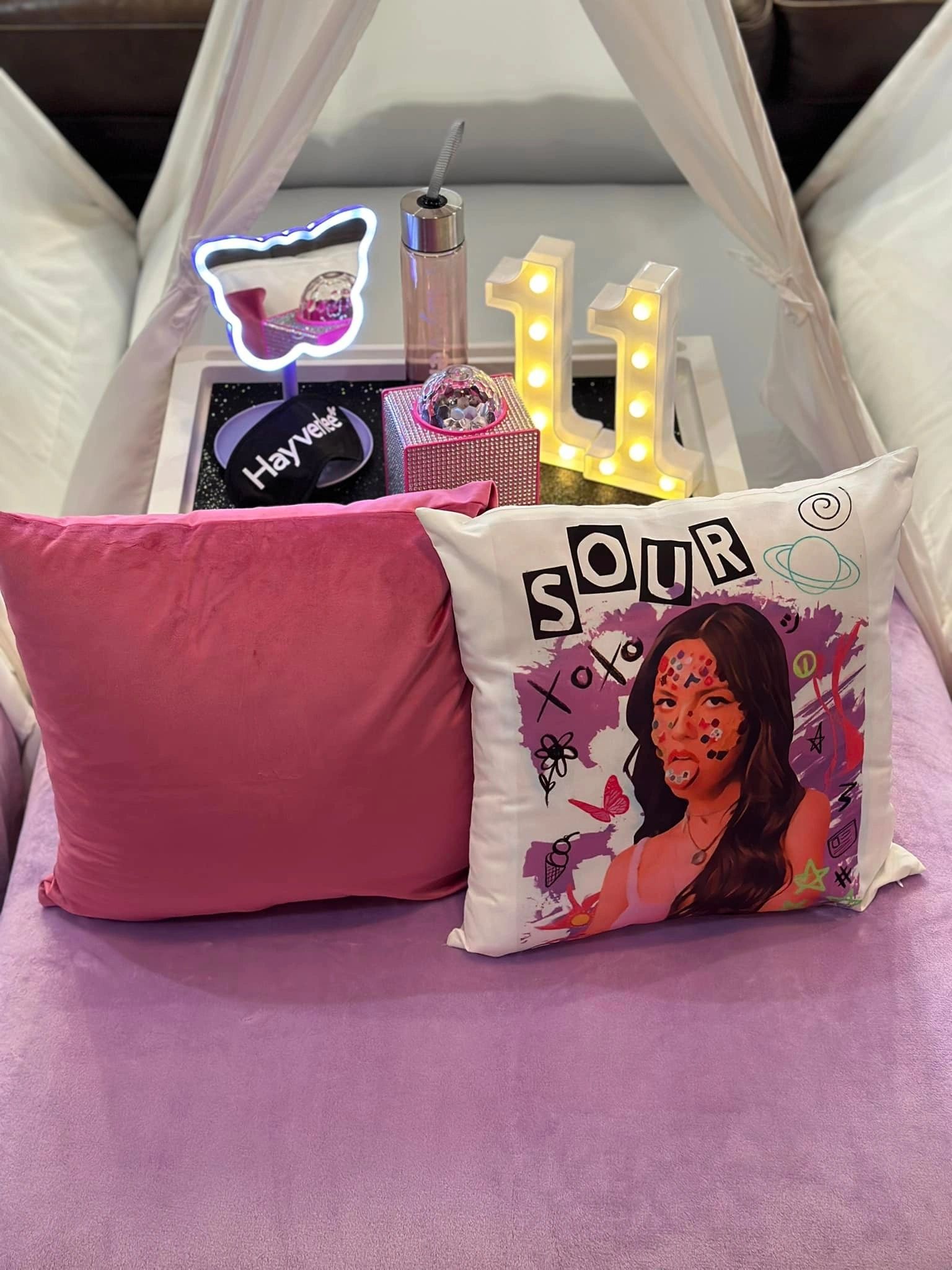 Cozy setup with pillows, LED lights, and a decorated water bottle on a soft purple blanket.