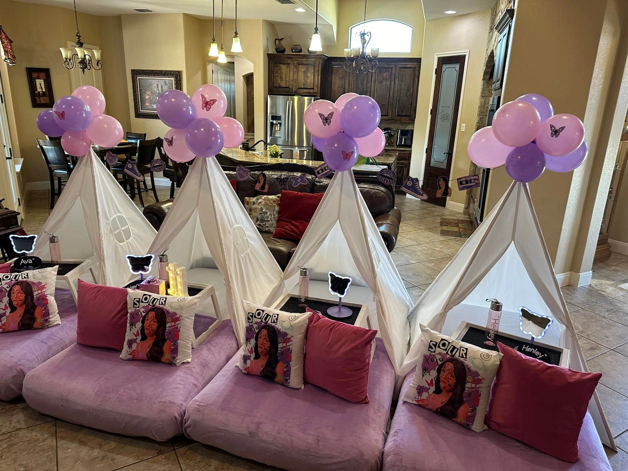Indoor party setup with teepees, purple and pink balloons, and themed cushions.