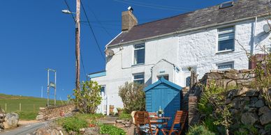 Arallt Holiday Cottage  from the garden with patio set and wine  on table. Blue shed in foreground.