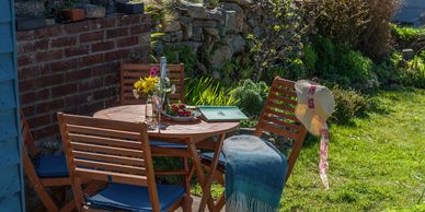 Garden table and chairs at Arallt Holiday Cottage with lap rug, hat, wine, flowers and strawberries