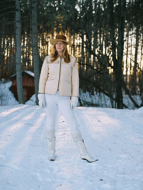 Woman in winter attire standing in snowy forest.