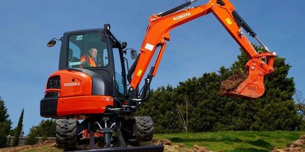 Orange Kubota excavator digging soil with operator inside.