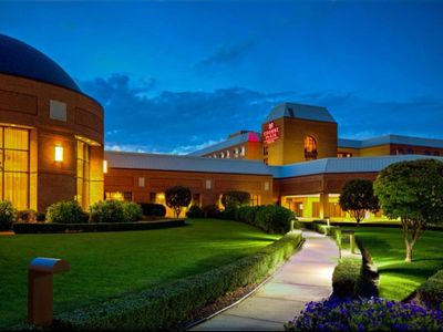 A well-lit hotel building at dusk with a manicured garden and pathway.
