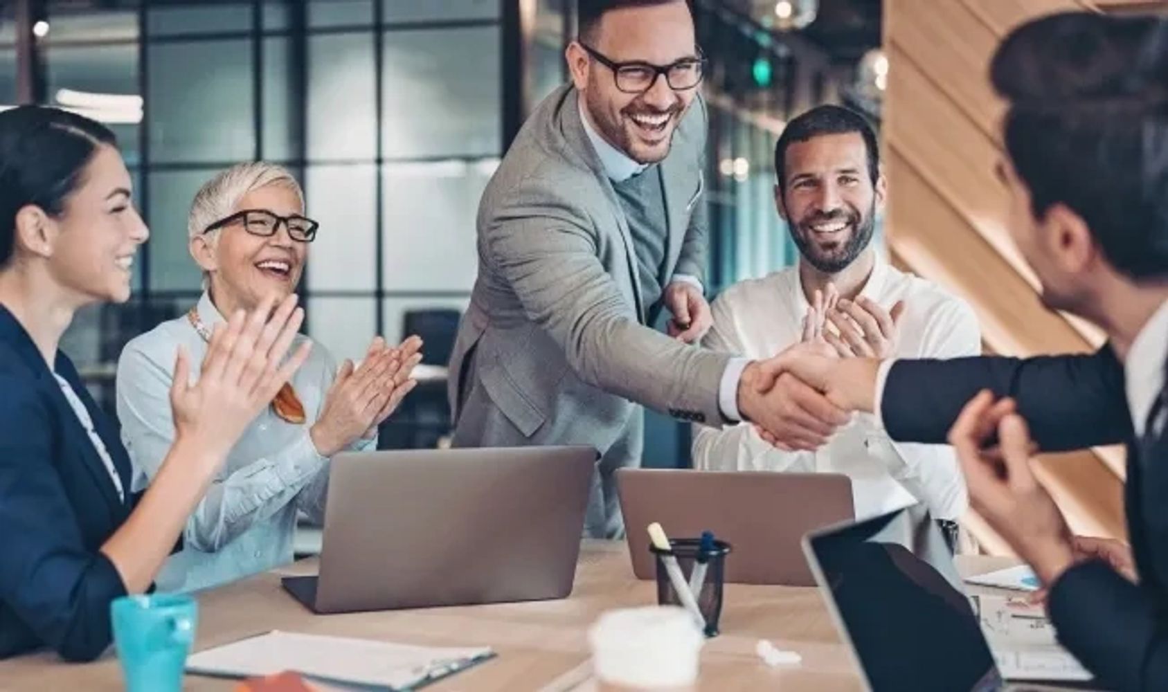 Business colleagues shaking hands and celebrating in a meeting room.