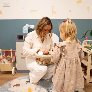 Woman and child engaged in an activity with a basket in a cozy playroom.