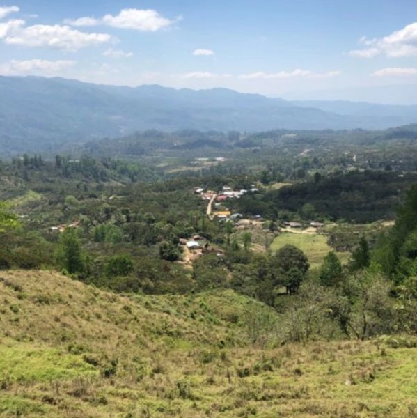 Scenic valley with scattered houses and distant mountains under a blue sky.