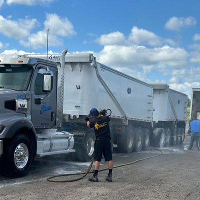 Workers washing a large dump truck outdoors on a sunny day.