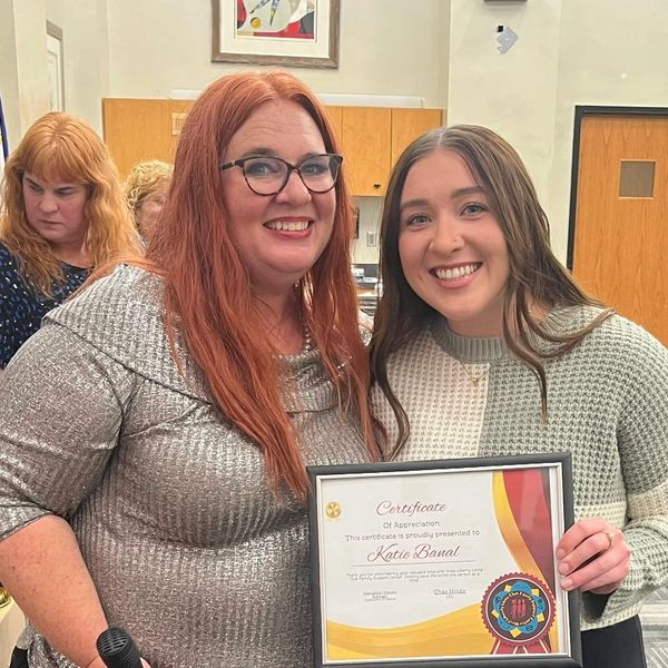 Two women smiling, one holding a certificate of appreciation.