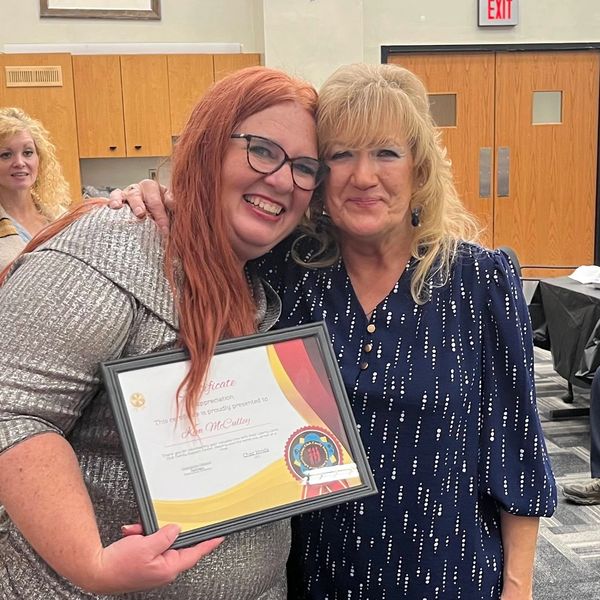 Two women smiling, one holding a framed certificate of appreciation.